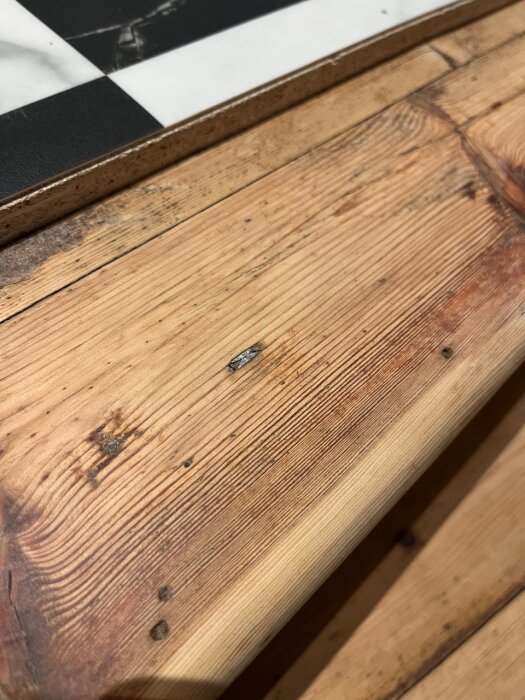 Ett träbord med synliga ådringar, närbild på struktur och skada. Checkerbräde i bakgrunden.