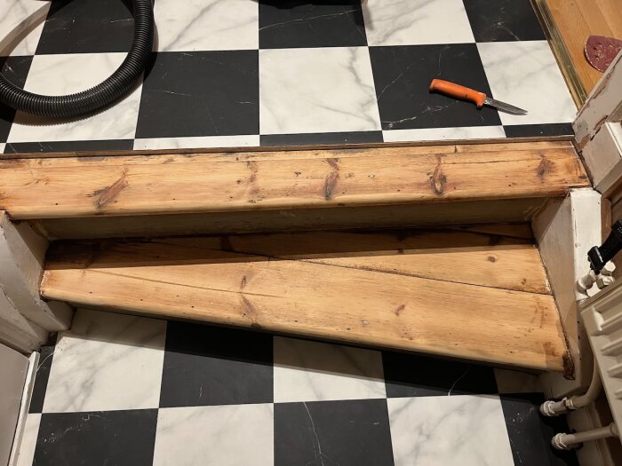 Trätrappa, svartvit rutigt golv, mejsel, reparation eller renovering pågår inomhus.