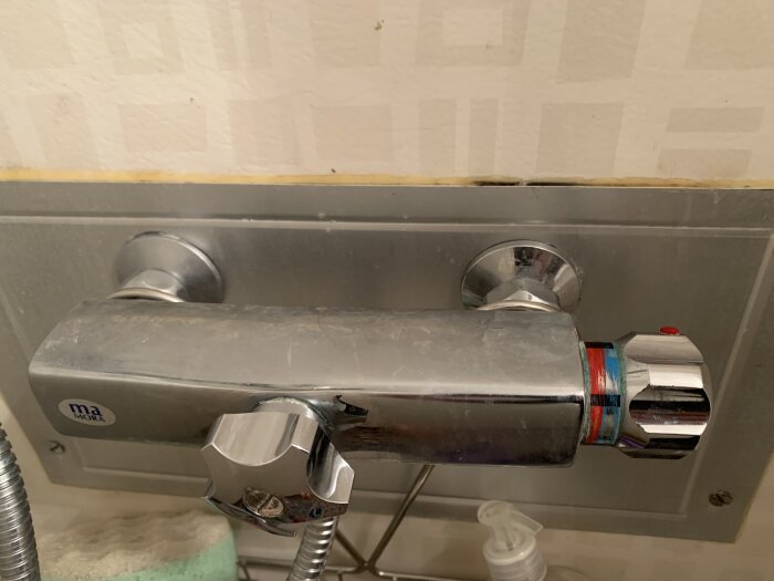 Blandare och temperaturreglage i ett badrum, använd och delvis kalkbelagd, med synlig svamp och tvålflaska.