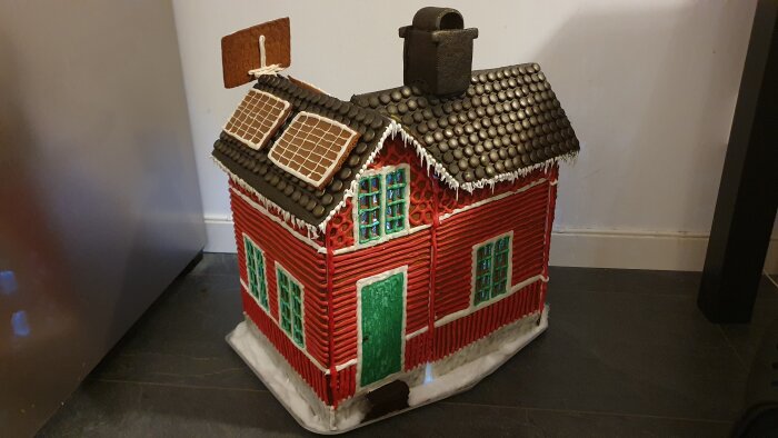 Modell av ett hus med pepparkakstak, röda väggar, och godisdekorationer på en bas.