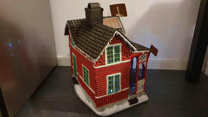 Modell av ett rött hus med vita snickerier, snöeffekt, chokladtakpannor och utsmyckning som liknar glasyr.