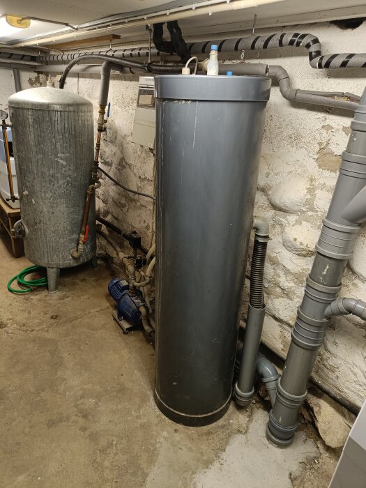 Två stora behållare, rör, elskåp och betongväggar i ett källarutrymme.