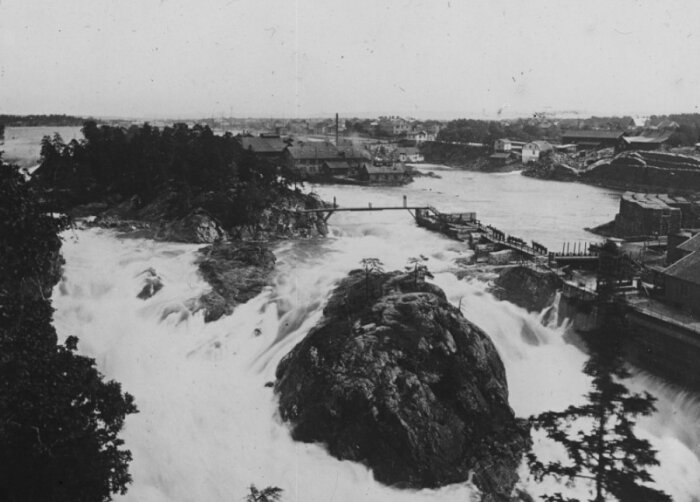 Svartvitt foto, forsande vatten, träbyggnader, broar, industriell känsla, historiskt, natur, öar, dramatisk flodström.