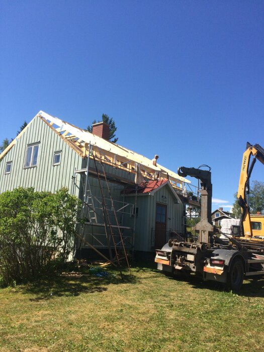 Hus under renovering, takbyte, byggnadsställning, grävmaskin, klar himmel, dagtid.