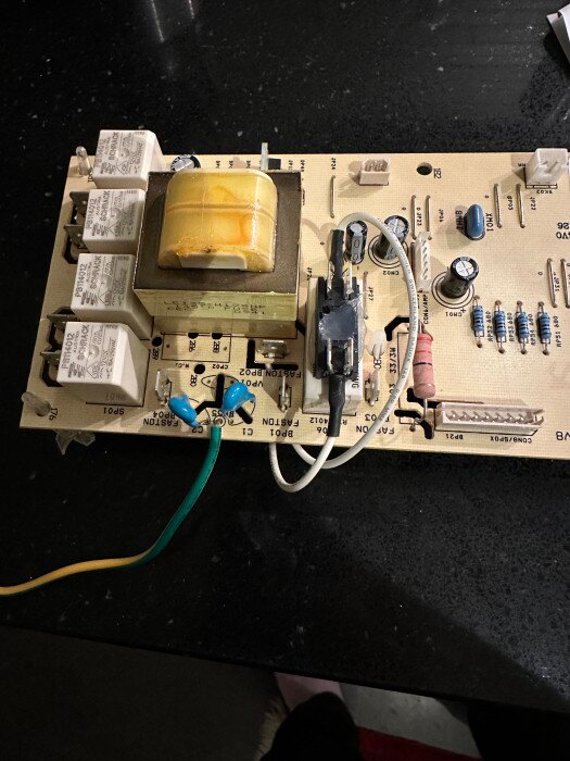 Kretskort med transformator, kondensatorer, motstånd, och reläer: elektronisk komponenter, bordsyta i bakgrunden.