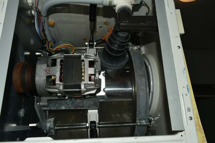 Inuti tvättmaskin, motor och ledningar synliga, demonterad, underhåll eller reparation, komplexa komponenter.