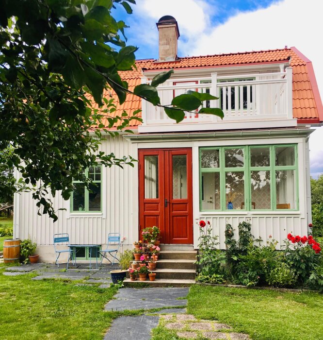 Idylliskt trähus, rött tak, veranda, blommor, grönska, lantlig charm, sommardag.