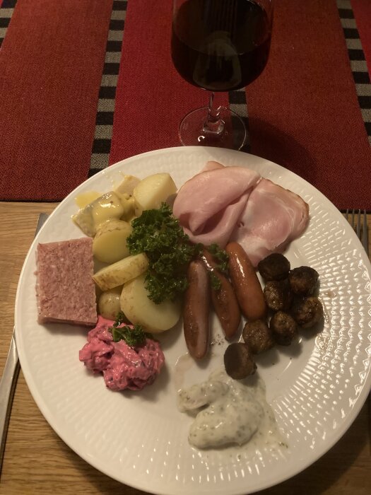 Ett måltidsstilleben: kokt potatis, skivad korv, prinskorv, köttbullar, rödbetssallad, pate, persilja och rödvin.