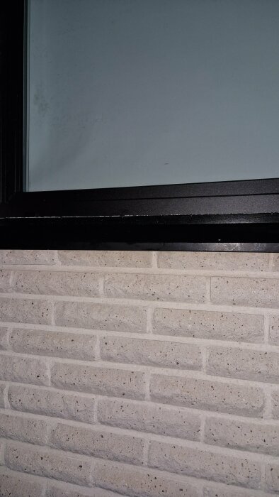 Ett fönster ovanför en vägg med ljust tegelmönster och en svart fönsterkarm nertill.