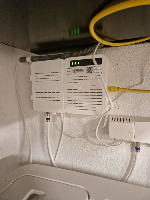 Fiberanslutningsbox med nätverkskabel och optisk kabel väggmonterad, indikatorlampor lyser grönt.