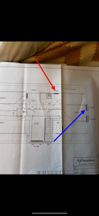 Arkitektonisk ritning av bostad, visar planlösning med mått och rum, document på A3-papper, röda och blåa pilar pekar.