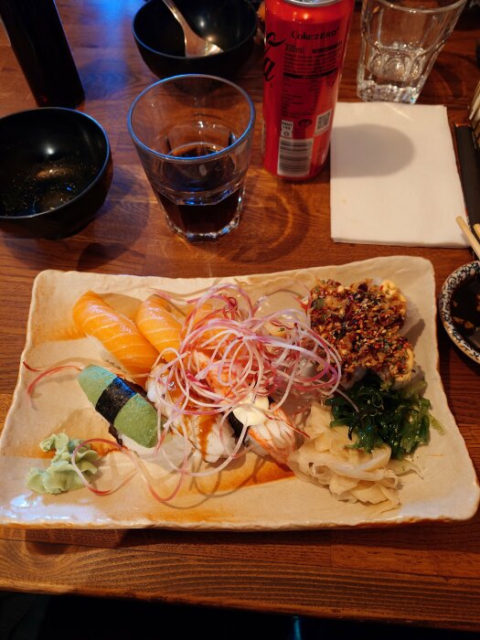 Sushi med lax, avokado, räkor, ål, sjögräs, ingefära; sojasås, Coca-Cola Zero, vatten, äten soppa, träbord.