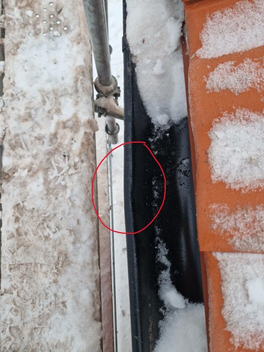 Bilden visar en svart rörledning mot en mur, inringad defekt, omgiven av snö och is.