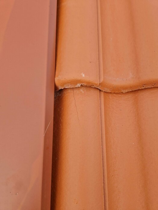 Närbild av terrakottafärgade takpannor med en spricka vid skarven.