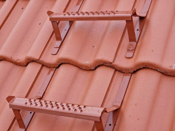 Tegelröda takpannor med en stege säkrad; småstenar på stegens steg; mörkgrå himmel ovan.