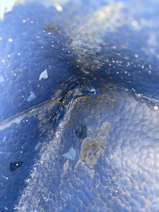 Blå yta med ljusreflektioner och strukturer som liknar is eller glas, oskarp bakgrund.