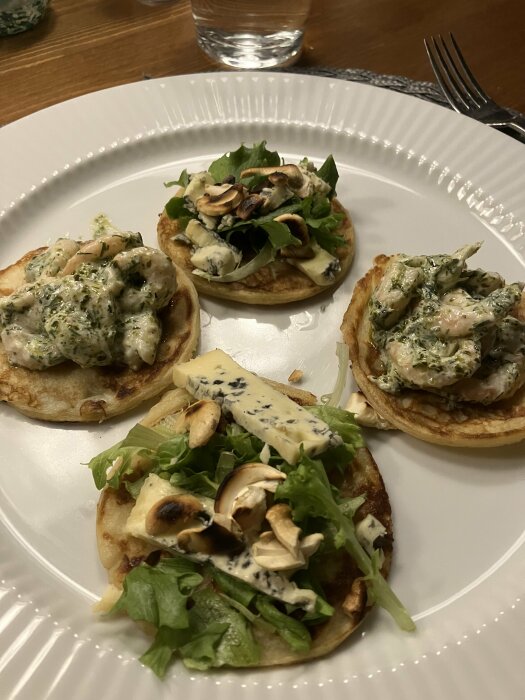 Tre små pannkakor med salladsblad, kantareller, blåmögelost och krämig sås på en vit tallrik.