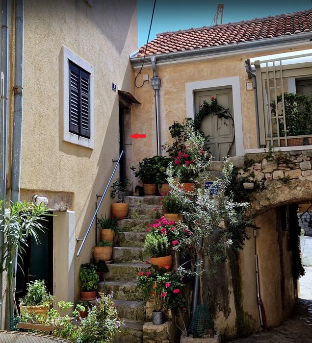 Mysig gränd, blommor, stentrappa, traditionella byggnader, medelhavsatmosfär, soligt, charmigt bostadsområde.