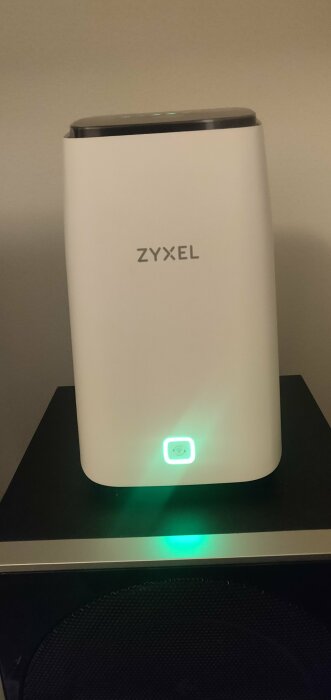 En vit Zyxel-enhet med ljus indikator på svart yta, troligen en router eller modem.