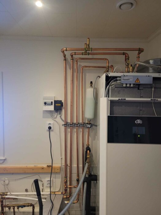 En värmepumpsanläggning med kopparledningar, installationsutrustning och elektriska komponenter mot en vit vägg.