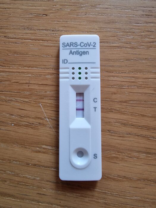 Ett positivt SARS-CoV-2 antigentest på träbakgrund.