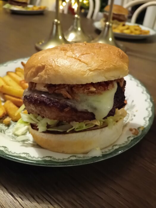 En saftig hamburgare med ost, pommes frites i bakgrunden, serverad på ett dekorerat porslinstallrik, hemtrevligt inredd bord.