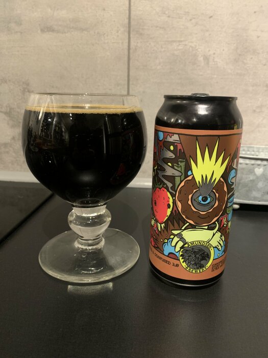 En ölburk och ett glas med mörkt öl på en grå bakgrund. Konstnärlig, färgglad etikett med monstermotiv.