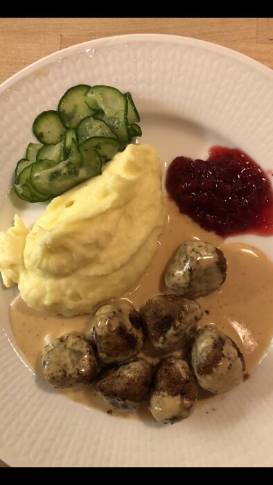 Tallrik med köttbullar, potatismos, gräddsås, lingonsylt och gurksallad; klassisk svensk maträtt.