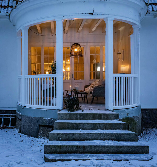 Mysig veranda med tända ljus, snöigt landskap, kvällshimmel, varm och välkomnande atmosfär.