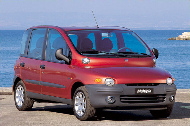 Röd Fiat Multipla vid havskant, två våningar med fönster, ovanlig design, parkerad utomhus under klar himmel.