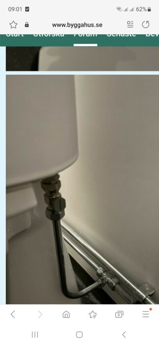 Vit lampskärm nära vägg, toalettpappershållare, smartphone webbläsarfönster med svensk webbsida "byggahus.se" öppen.
