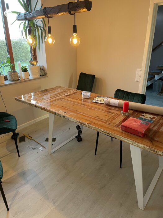 Matbord och stolar, rustik lampa, fönster, växter, verktyg och byggmaterial på golvet.