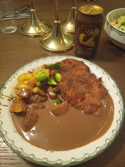 Middag med schnitzel, potatis, brunsås, broccoli, ölburk "Falcon", bakgrund med ljusstake och salladsskål.