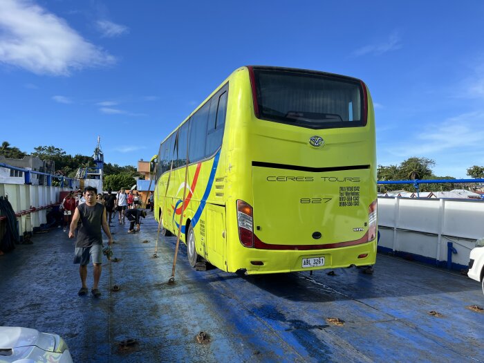 Gul buss på en färja, människor som går, solig dag, blå himmel.