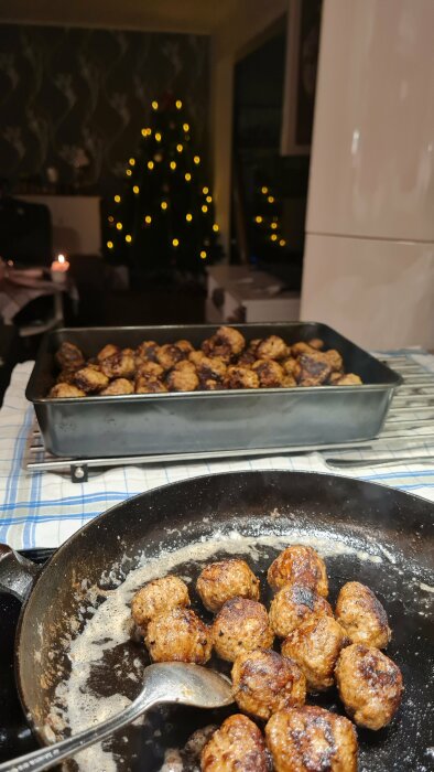 Stekta köttbullar i panna, mer i form, julgran med ljus i bakgrunden. Mysig hemmiljö.