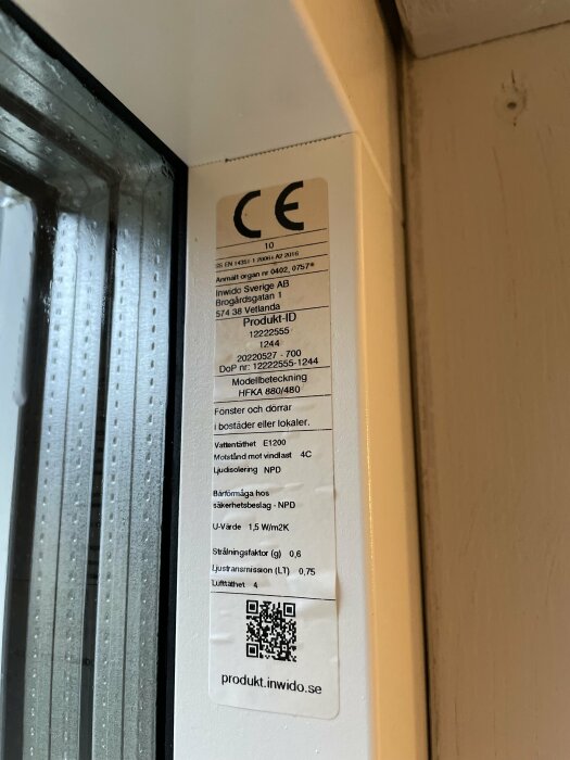 Etikett på fönsterkarm med CE-märkning och tekniska specifikationer, inklusive QR-kod och vattentäthetsvärden.