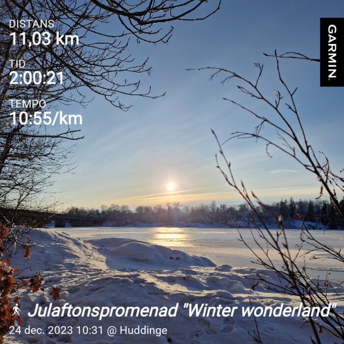 Vintersol över snötäckt landskap, grenar i förgrunden, löprunda-data, Juldagens morgonpromenad i Huddinge.