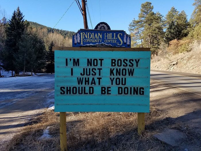 Skylt med text: "I'm not bossy, I just know what you should be doing", natur och väg i bakgrunden.