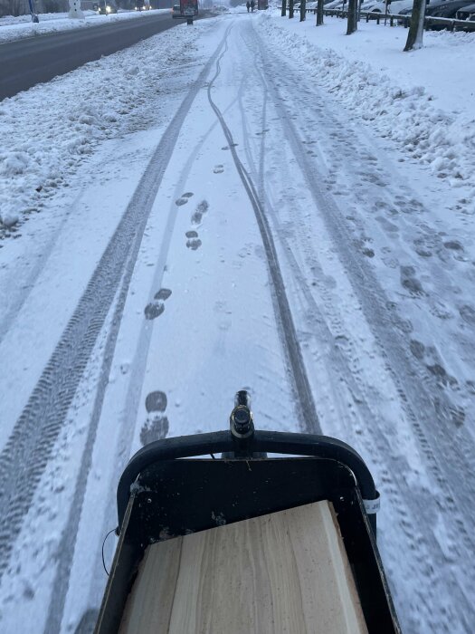 Cykelkorg, snöig cykelbana, fotspår, bildäcksspår, vinter, träd, gatlyktor, tidig morgon eller skymning, kyligt.