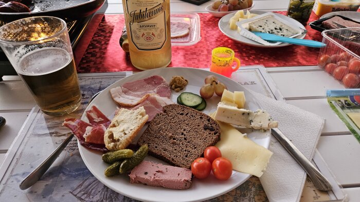 En måltid med ost, bröd, kött, öl, akvavit och små tillbehör på ett dukat bord.