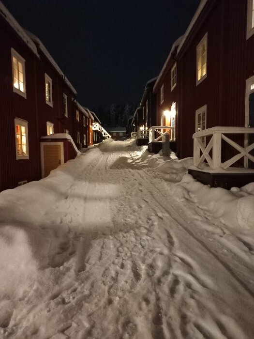 Snötäckt gata, traditionella röda trähus, vintertid, kväll med gatubelysning.