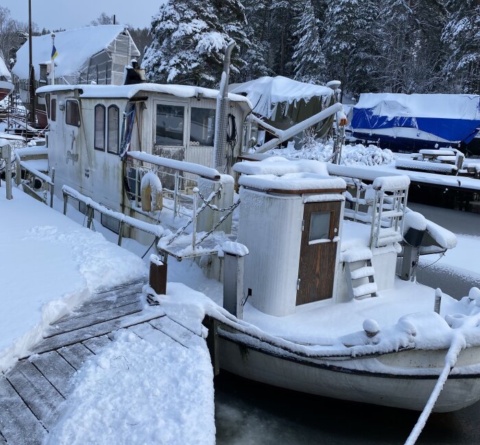 Vintertid vid en brygga; snötäckt båt och förtöjningsplats, lugn och stilla atmosfär.