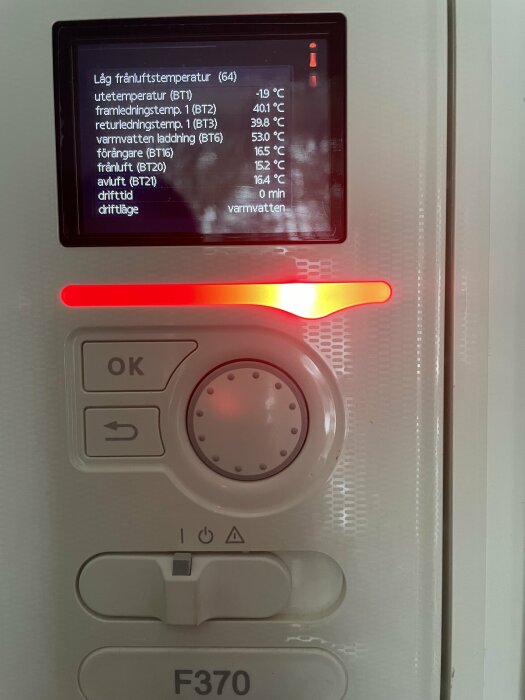 Värmepumpsdisplay med temperaturvärden och status, röd indikatorljus och styrenhet nedanför. F370 modell, driftlägesindikator tänt.