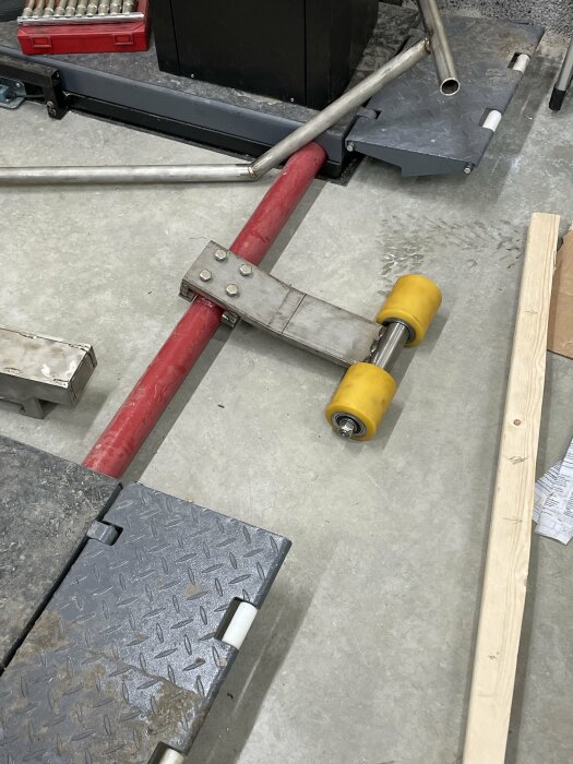 Verkstadsinredning med stålrör, verktygslåda och olika byggmaterial på ett grått golv.