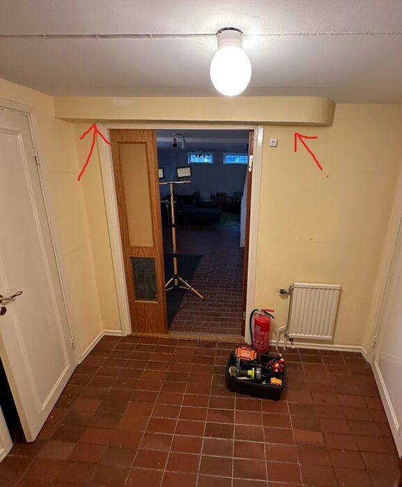 Interiör av en korridor med tegelgolv, en öppen dörr, brandvarnare och verktygslåda.