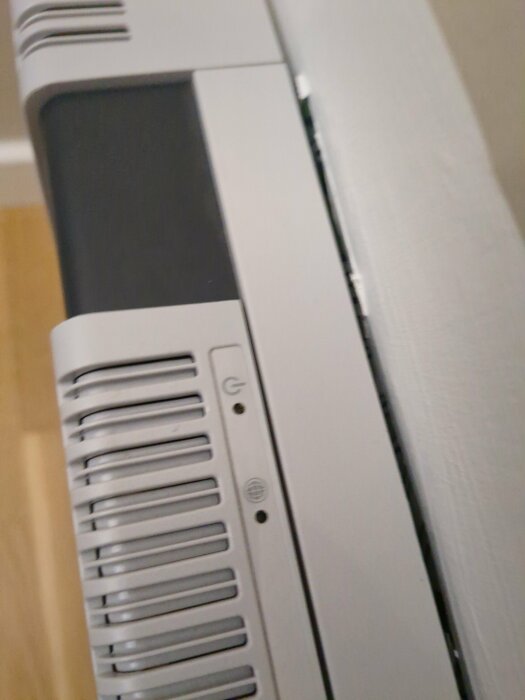Datorchassi delvis i fokus med ventilationsgaller, knapp och logotyp. Vit bakgrund, närbild.