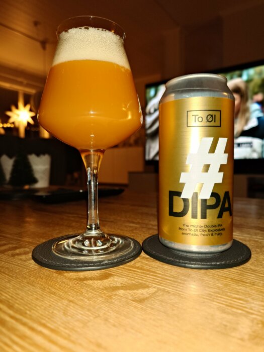 Ett glas öl och en burk med texten "#DIPA" framför en TV i ett vardagsrum.