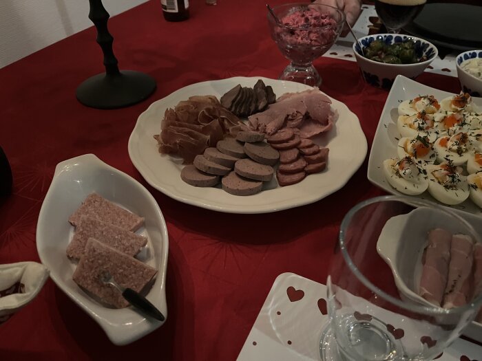 Julbord med diverse kötträtter, ägghalvor och tilltugg på röd duk.