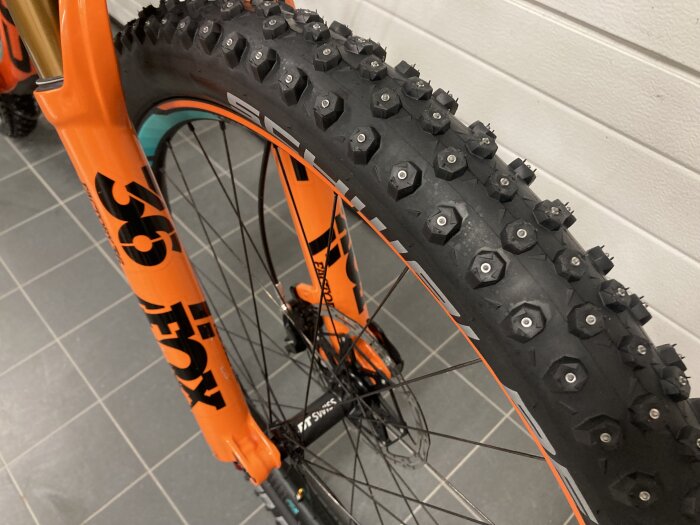 Orange cykelgaffel och däck med dubbar för grepp på is och snö.