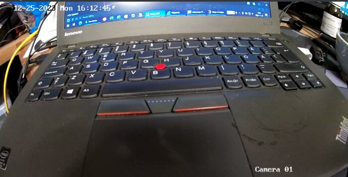 Lenovo ThinkPad bärbar dator med tangentbord, TrackPoint, skärmdatum och tid, övervakningskamera vy. Dustig yta.